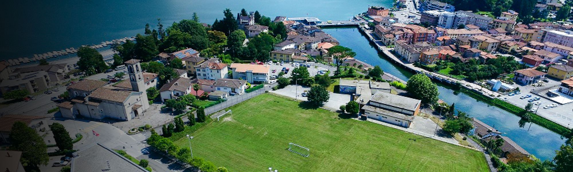 Fußballplatz in der Schweiz, umgeben von Häusern und einem Fluss, mit Blick auf den See.