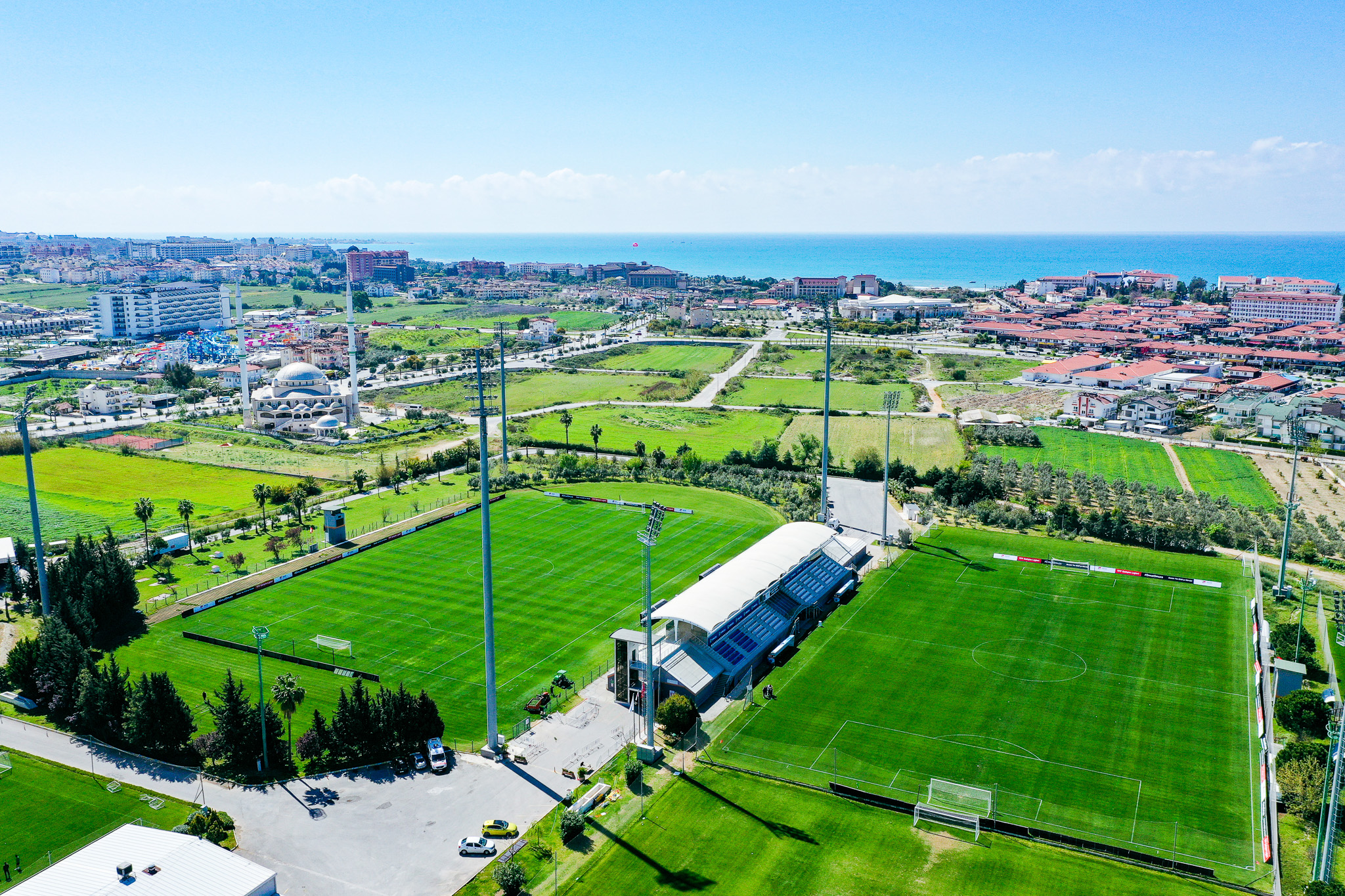Fußballtrainingslager in der Türkei mit zwei gepflegten Fußballplätzen, umgeben von grüner Landschaft und nahe der Küste.