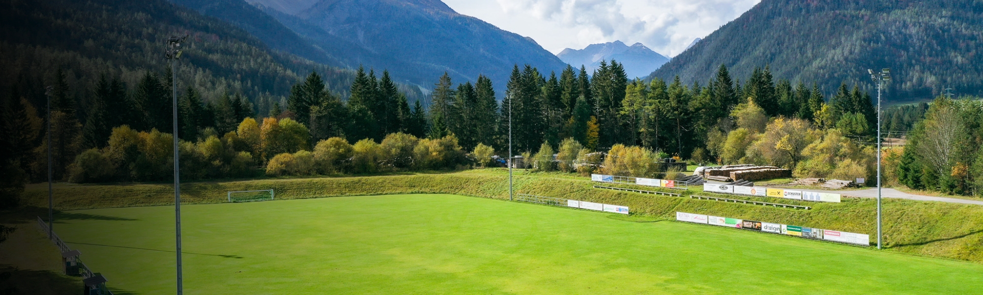 Fußballplatz in idyllischer Berglandschaft in Tirol, mit Blick auf Wälder und die Alpen im Hintergrund.
