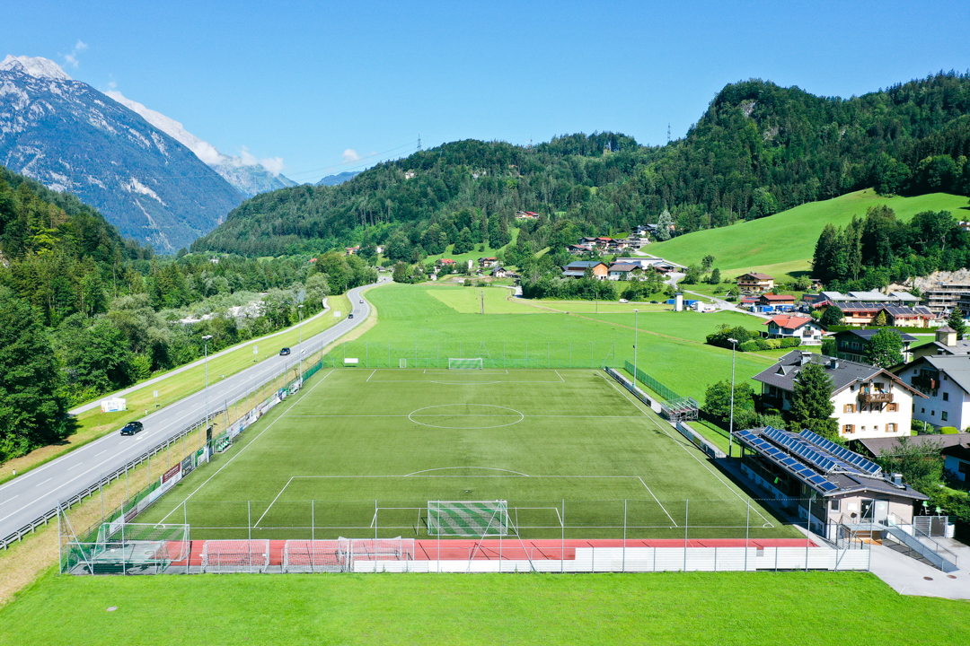 Fußballplatz in den österreichischen Alpen, umgeben von Bergen und Wiesen.